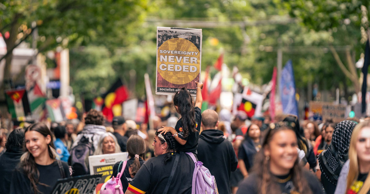 Crowd at an Invasion Day rally holding a sign saying Sovereignty Never Ceded